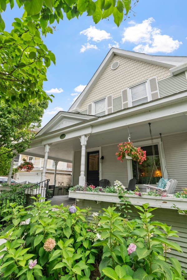 A traditional house with a scalloped roof and vibrant flowers on the porch and in the garden.