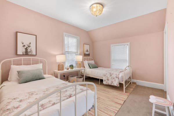 A bedroom featuring two white metal beds, soft pink walls, and playful decor.