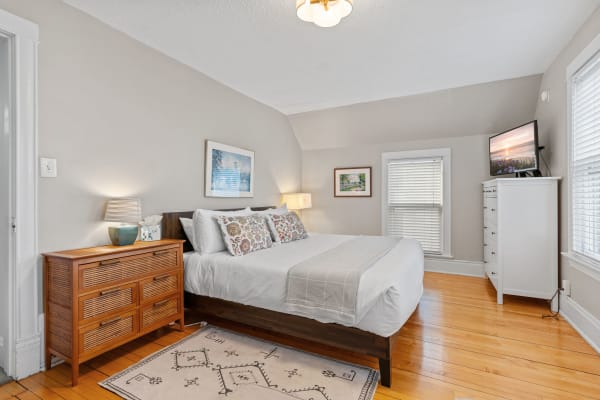 Neatly arranged bedroom with a large bed, wooden dresser, and natural light.