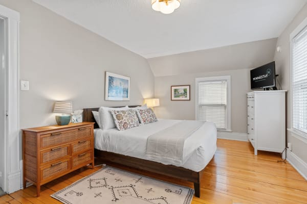 Cozy bedroom featuring a comfortable bed, wooden dresser, and natural light from windows.
