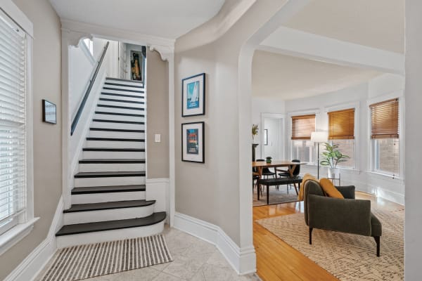 A cozy entryway featuring a staircase and a stylish living area with a green sofa and wooden dining table.