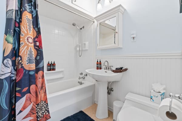 A bright bathroom with a floral shower curtain, pedestal sink, and modern decor.