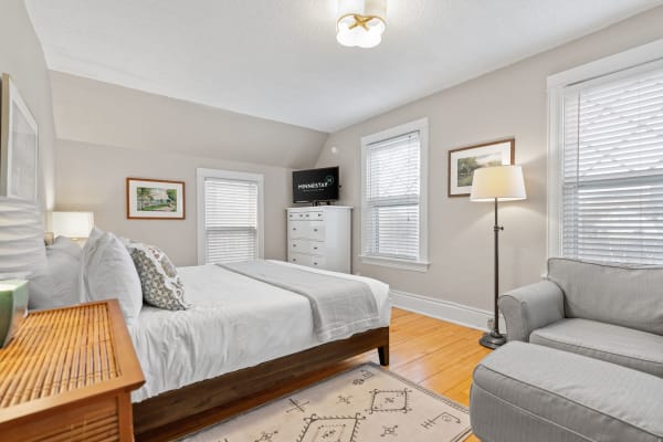 Cozy bedroom with a queen-sized bed, gray couch, and framed artwork.
