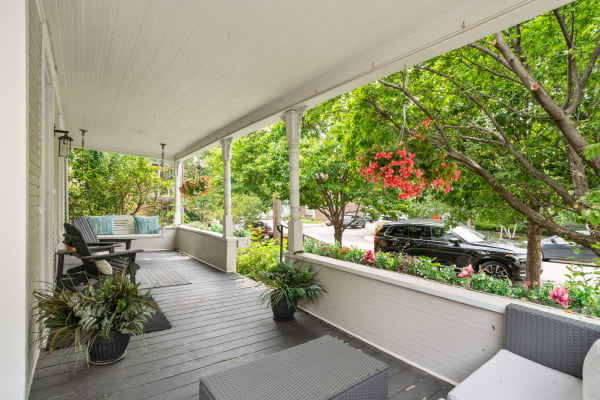 Front porch featuring black rocking chairs, potted plants, and colorful hanging flowers.