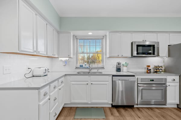 A bright kitchen with white cabinets, gray countertops, and stainless steel appliances.
