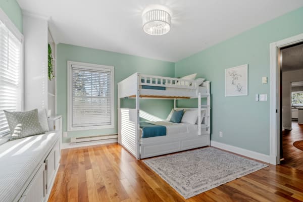 Bright bedroom with mint green walls, a white bunk bed, and a window seat.