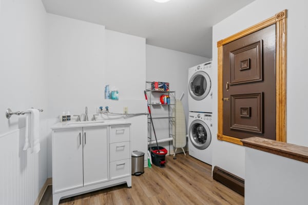 A bright laundry room with white cabinets, a double basin sink, stacked washer and dryer, and a towel rack.