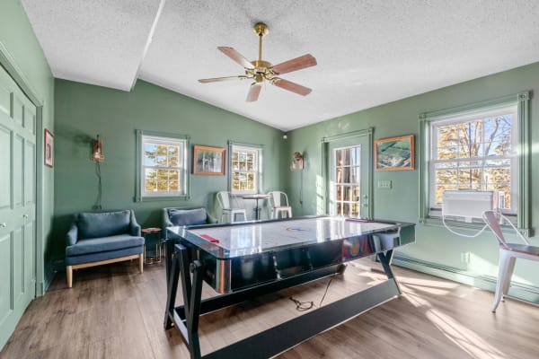 A green recreational room featuring an air hockey table, blue chairs, and bright windows.