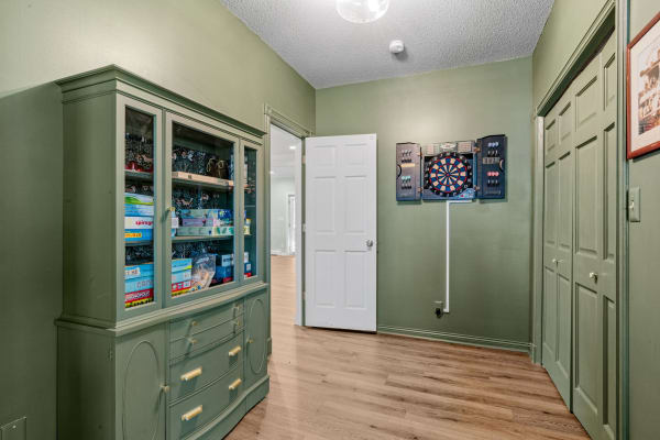 A hallway with green walls, a cabinet displaying board games, and a dartboard on the wall.