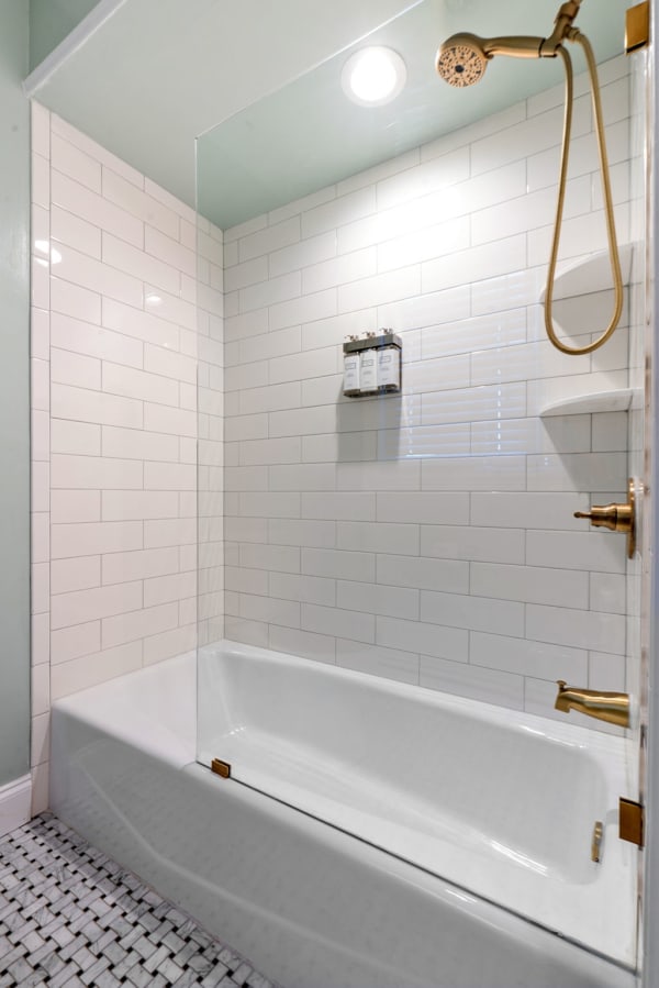 Contemporary shower area featuring white subway tiles, brass fixtures, and mosaic flooring.