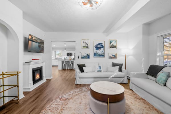 A modern living room featuring light sofas, a round coffee table, and a flat-screen TV above a fireplace.