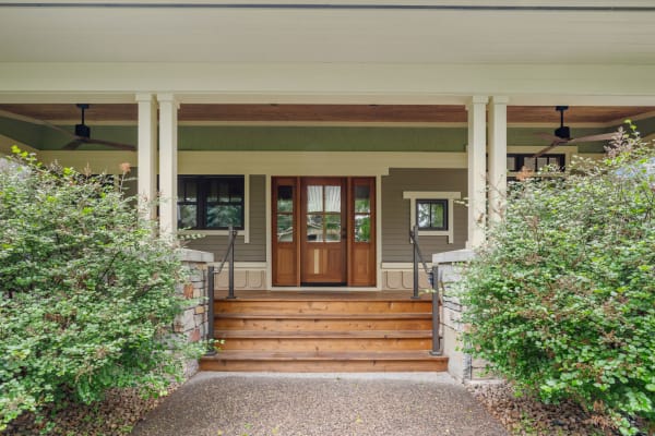 Front porch of a home with wooden double doors and surrounding shrubs.
