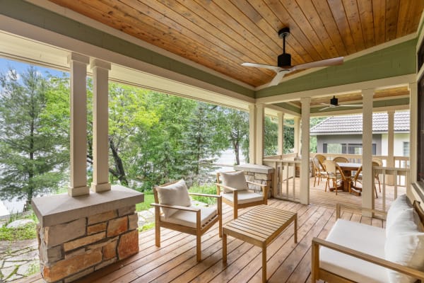 A cozy porch with wooden flooring, stone columns, and comfortable seating overlooking greenery.