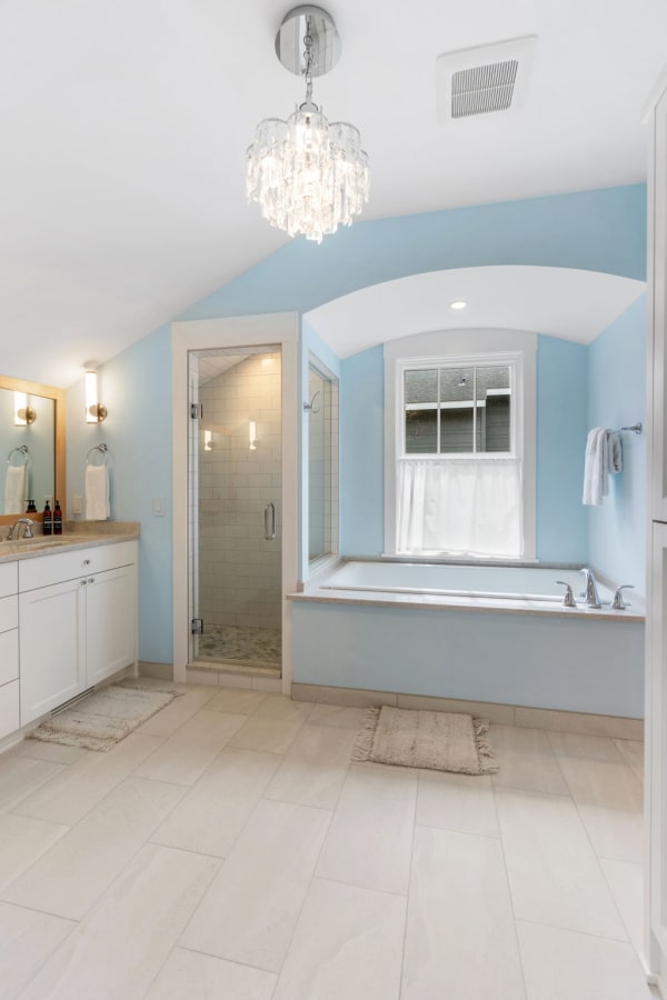 Modern bathroom with light blue walls, a chandelier, shower, and bathtub.