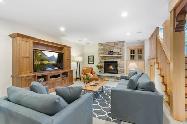 A warmly decorated living room featuring a stone fireplace, gray sofas, and an entertainment center.