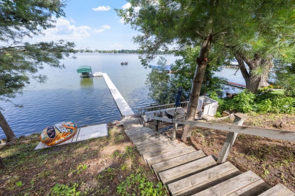 Wooden steps leading down to a calm lake with a dock and an inflatable tube nearby.