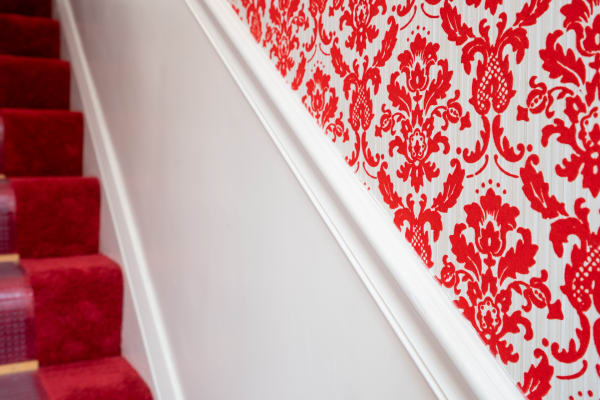 Staircase with red damask wallpaper and red carpet.