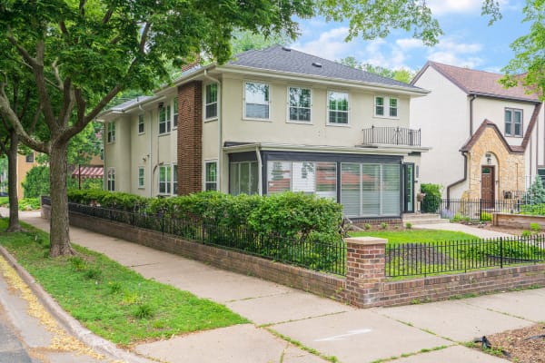 Two-story house with a hedged yard, brick elements, and large windows, next to another home.
