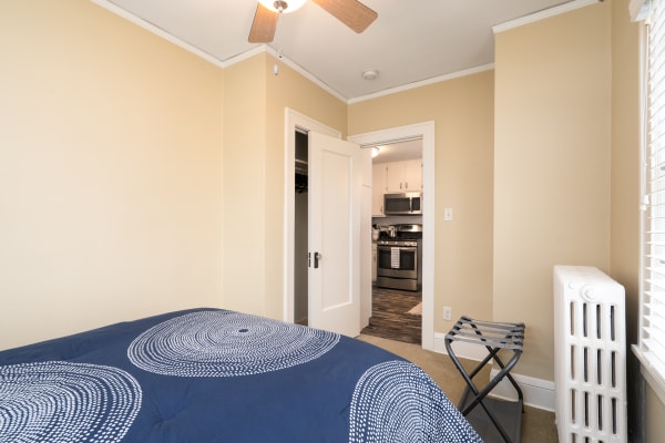 A bedroom with a bed, radiator, and doorway leading to a kitchen.