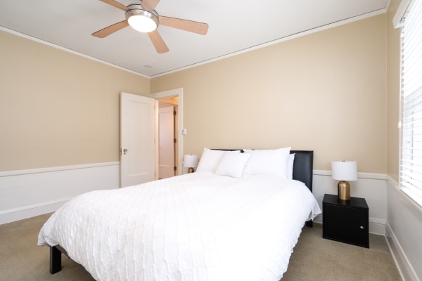 Modern bedroom with a white quilted bed, black nightstand, and ceiling fan.