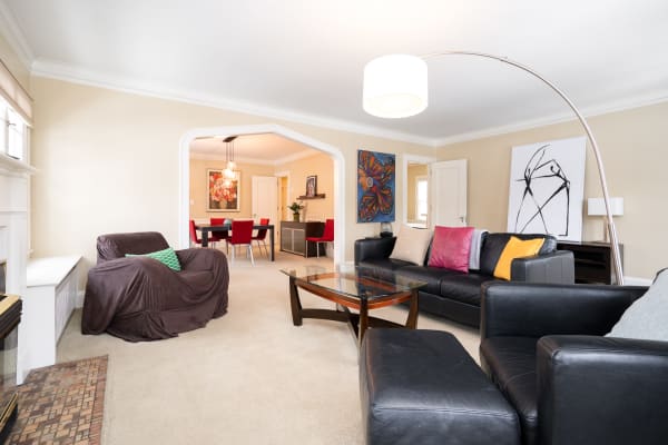 Cozy living room featuring a leather sofa, colorful pillows, and artwork, with an open archway leading to a dining area.