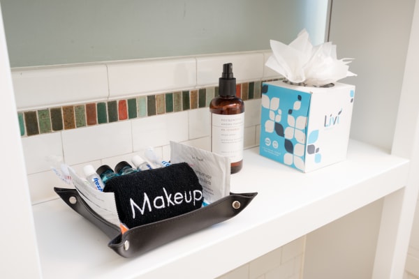 Bathroom shelf with organized personal care items including a black towel, small bottles, and a room spray.