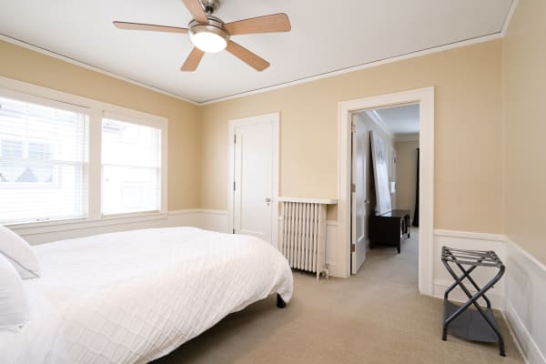 A minimalist bedroom with a bed, ceiling fan, and soft beige walls, enhancing the tranquil atmosphere.