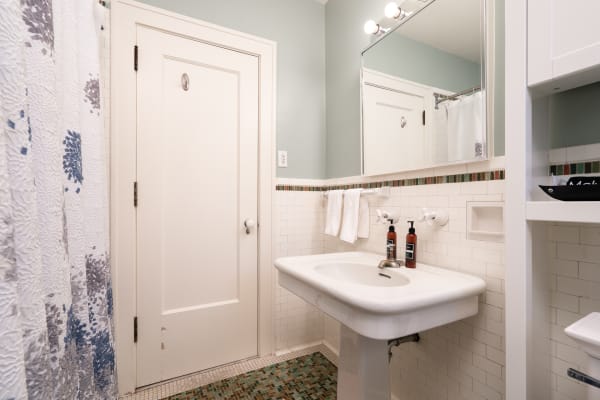 A clean and modern bathroom with a white sink, textured shower curtain, and mosaic floor tiles.