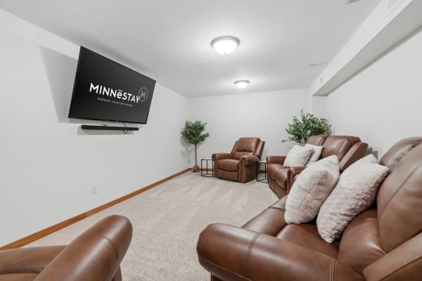 A room with brown recliners, a mounted TV displaying a logo, and plants in the corners.