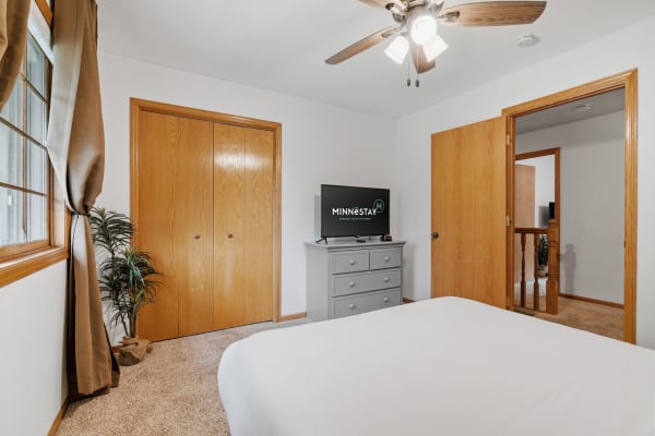 Cozy bedroom with a television, dresser, window, and two wooden doors.
