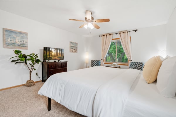 Inviting bedroom with a white bedspread, television, and natural light from a window.