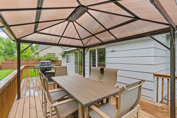 Outdoor dining area with a gazebo and grill on a wooden deck.
