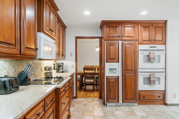 Interior view of a kitchen with wooden cabinets, modern appliances, and a dining area visible in the background.