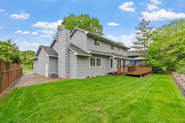Gray two-story house with wooden deck and landscaped yard.