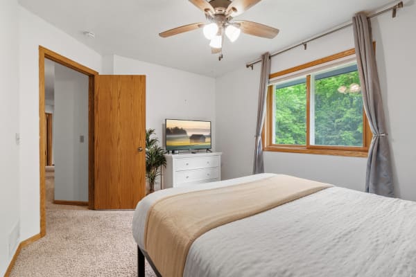 Cozy bedroom featuring a bed, dresser, and a large window with greenery outside.