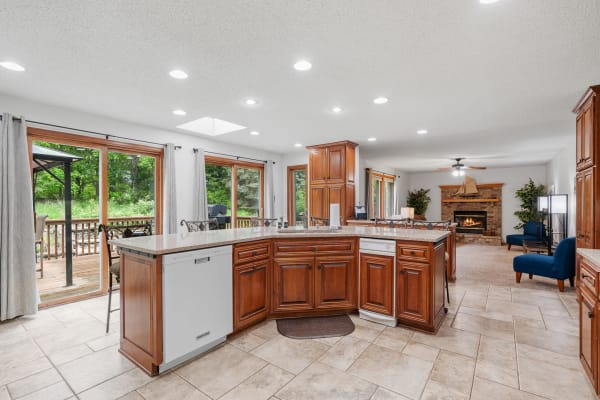 Spacious kitchen with wooden cabinetry, granite countertops, and a view of lush greenery through large windows.