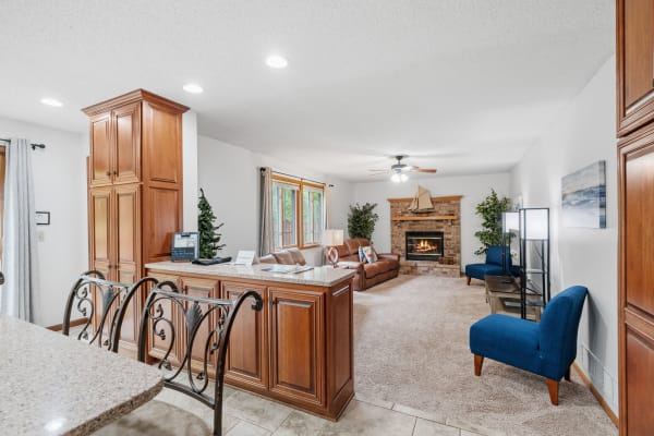 Spacious living room with a fireplace, blue chairs, and a view of the kitchen area.