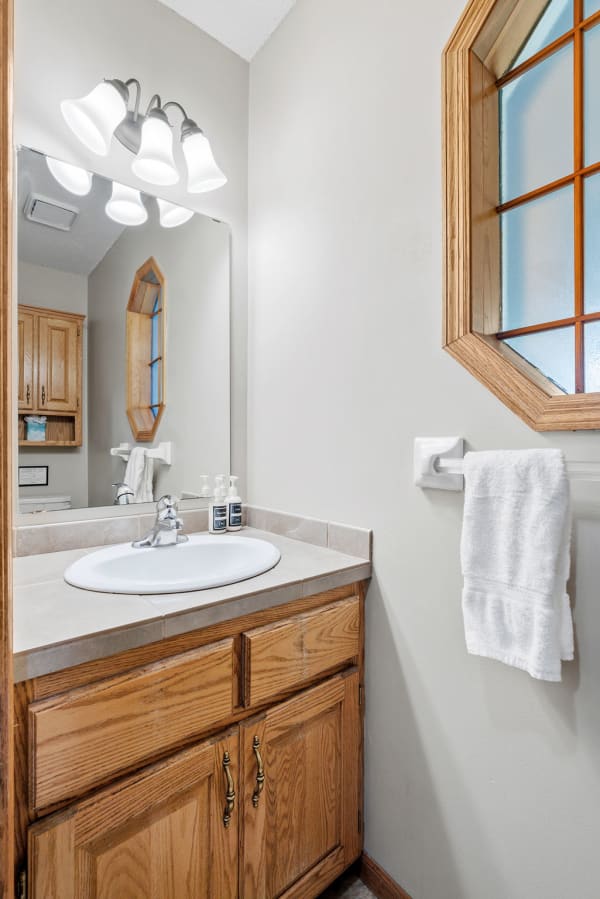A cozy bathroom with an oval sink, wooden cabinets, and an octagonal window.