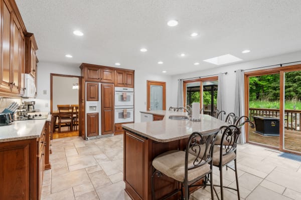Modern kitchen with wooden cabinetry, large island, and outdoor deck visible through sliding doors.