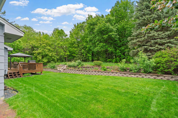 View of a backyard featuring a wooden deck, vibrant lawn, and green trees.