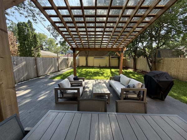 Outdoor patio with a wooden pergola, modern furniture, and green lawn.