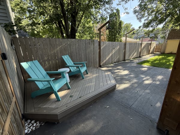 A tranquil outdoor space with turquoise Adirondack chairs, a wooden deck, and green grass.