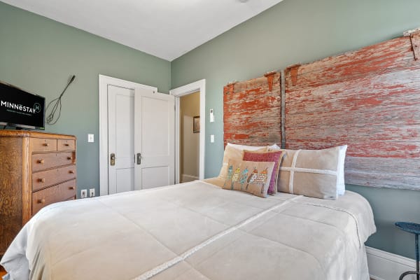 Cozy bedroom with a weathered wooden headboard, beige quilt, and a vintage dresser.