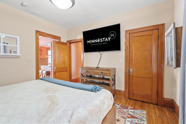 A cozy bedroom with a bed, wooden doors, and a TV displaying the MINNESTAY logo.