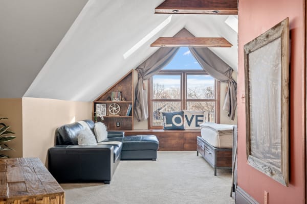 Bright attic room with a black leather sofa, large window, and decorative elements.
