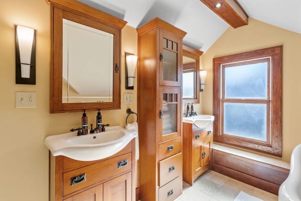A stylish bathroom featuring wooden cabinetry and dual sinks with a warm yellow wall backdrop.