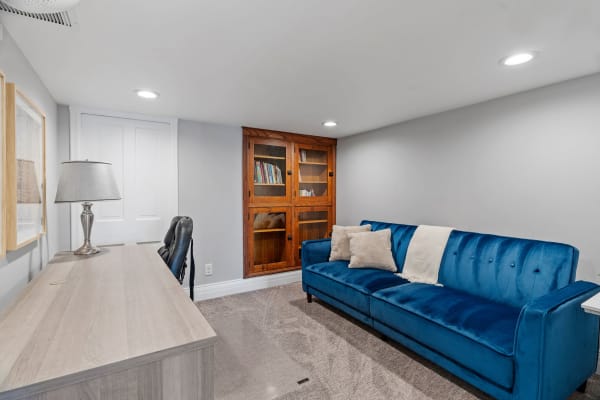 A cozy room with a blue velvet sofa, desk, lamp, and bookshelf.