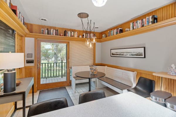 A dining nook featuring a black table, white seating, and bookshelves above, with a view outside.