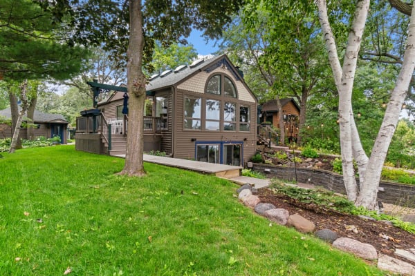 Lakeside cabin with large windows, wooden deck, and green grass.