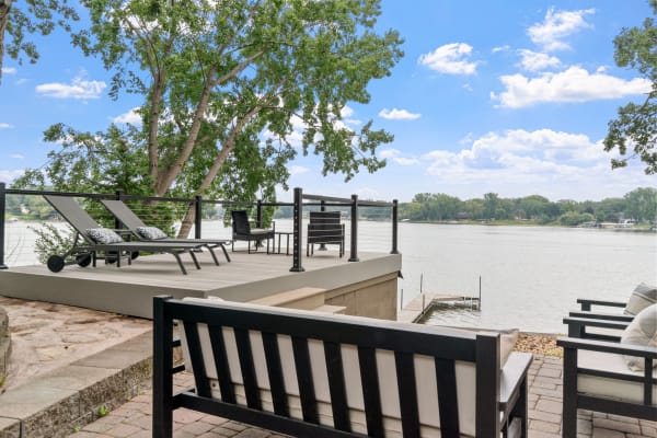 A modern deck with lounge chairs overlooking a calm lake under a blue sky.